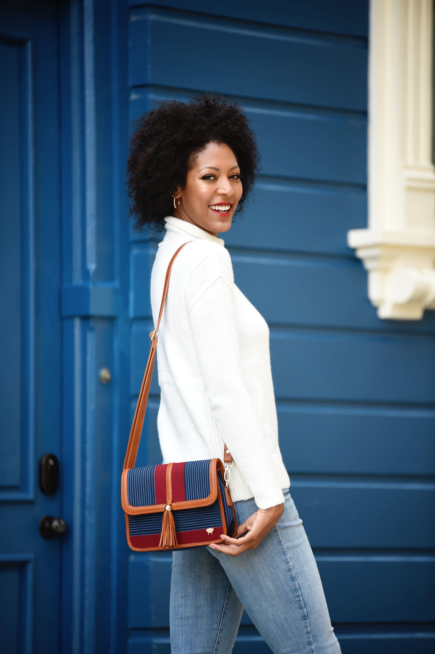 African-American model smiling at the camera, carrying an Olori Tola Maiden Crossbody bag in brown